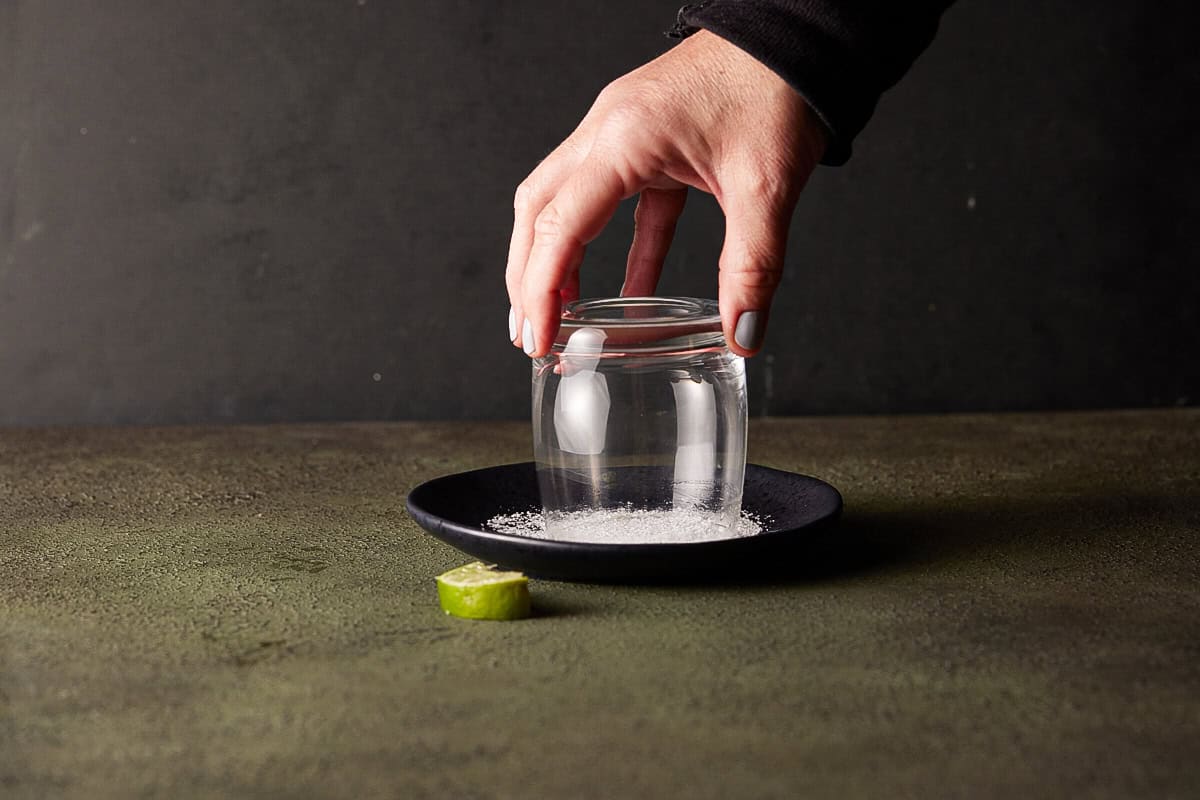 Hand holding a lowball glass and rimming the glass with salt from a plate.