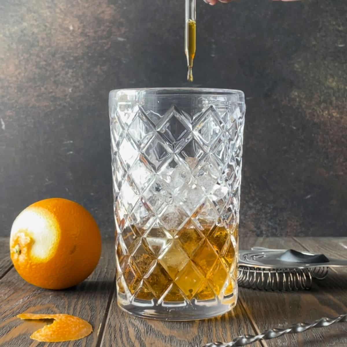 Hand dropping bitters into the mixing glass for an añejo tequila old fashioned cocktail.