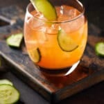 Aperol gin cocktail on dark background with cucumber slices.