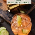 two low ball glasses filled with ice and aperol gin drink with slices of cucumber and lime wedges on side.