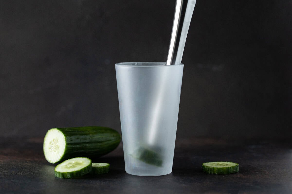 Cocktail shaker with cucumber slices and muddler.