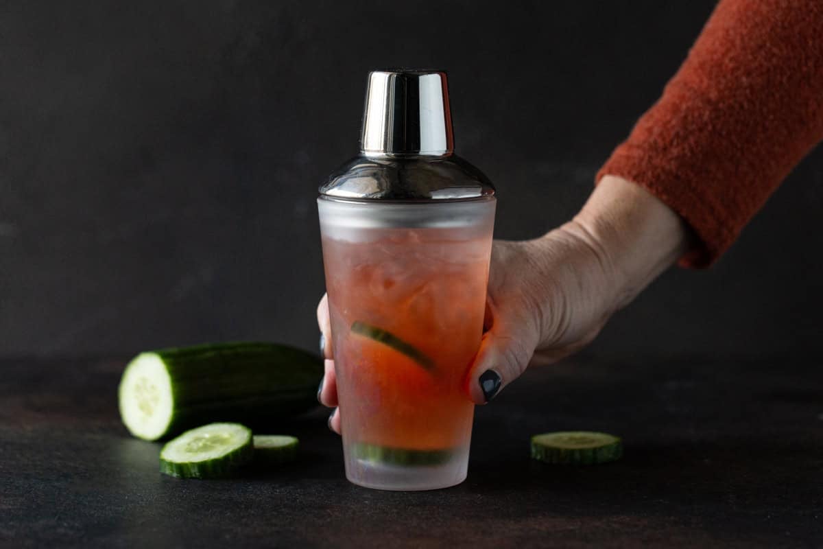 Hand on shaker filled with aperol, gin and lime juice.