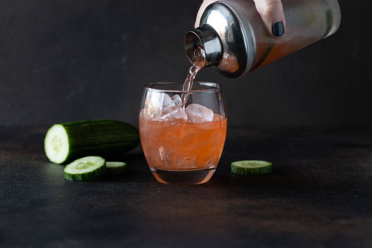 Straining aperol gin cocktail into glass filled of ice.