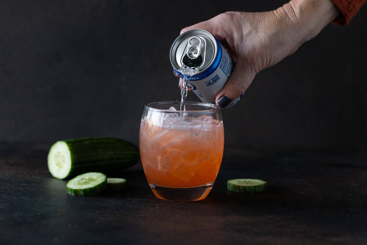 Pouring club soda into cocktail filled glass.