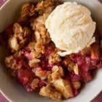 apple rhubarb crisp in a bowl with a scoop of vanilla ice cream.