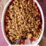 Apple Rhubarb crisp in a white baking dish with a scoop out.