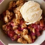 A white bowl filled with a serving of Apple Rhubarb Crisp and a single scoop of ice cream on time.
