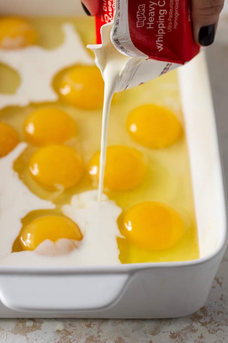 Eggs cracked in a white casserole dish with cream poured over the top.