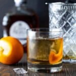 Lowball glass filled with añejo tequila old fashioned cocktail next to a cocktail mixing glass and a bottle of añejo tequila.