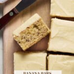 Banana bars with Cream Cheese Frosting on a wooden cutting board with a spreader.