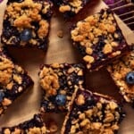 Eight blueberry crumble bars on brown parchment paper on a wire cooling rack.