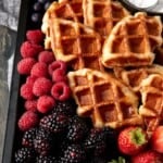 Croissant waffles (croffles) on a dark sheet pan with fresh berries and powdered sugar.