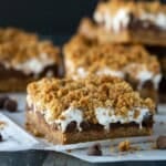 A cluster of 4 baked s'mores bars on white parchment paper with chocolate chips and graham cracker crumbs.
