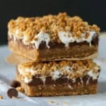 Two baked s'mores bars stacked on top of each other and separated by brown parchment paper.