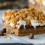 A gooey baked s'mores bar on a piece of white parchment paper with chocolate chips.