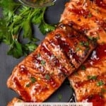 Maple ginger glazed grilled sockeye salmon fillets on a dark sheet pan with a small bowl of crushed red pepper flakes.