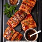 Grilled sockeye salmon fillets on a black sheet pan with small bowls of red pepper flakes and a maple ginger glaze.