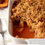 Peach crumble with a spoonful removed and fresh peaches.