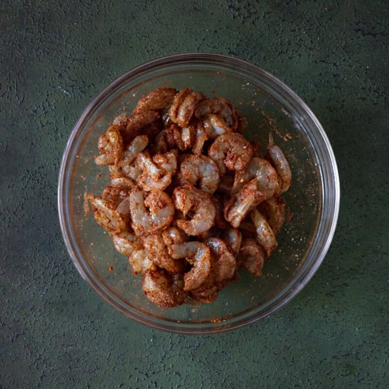 Raw shrimp in bowl with seasoning on it.
