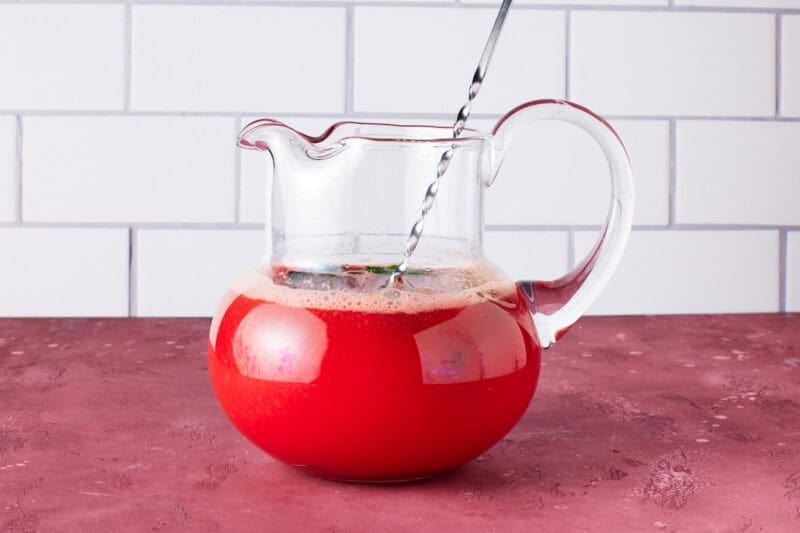 Watermelon mojitos in a glass pitcher with a bar stirring spoon.