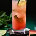 A watermelon mojito in a highball glass on a dark coaster.