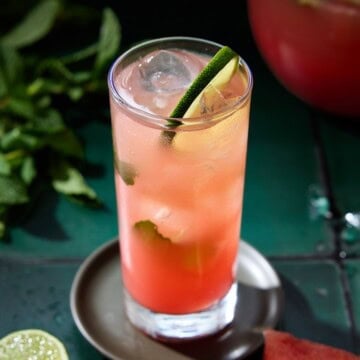 A single highball glass filled with watermelon mojito and garnished with a lime wheel and fresh mint.