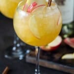 Wine glasses of apple cider sangria, garnished with apple slices and a cinnamon stick.