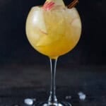 A tall wine glass filled with apple cider sangria, apple and pear slices and a cinnamon stick.
