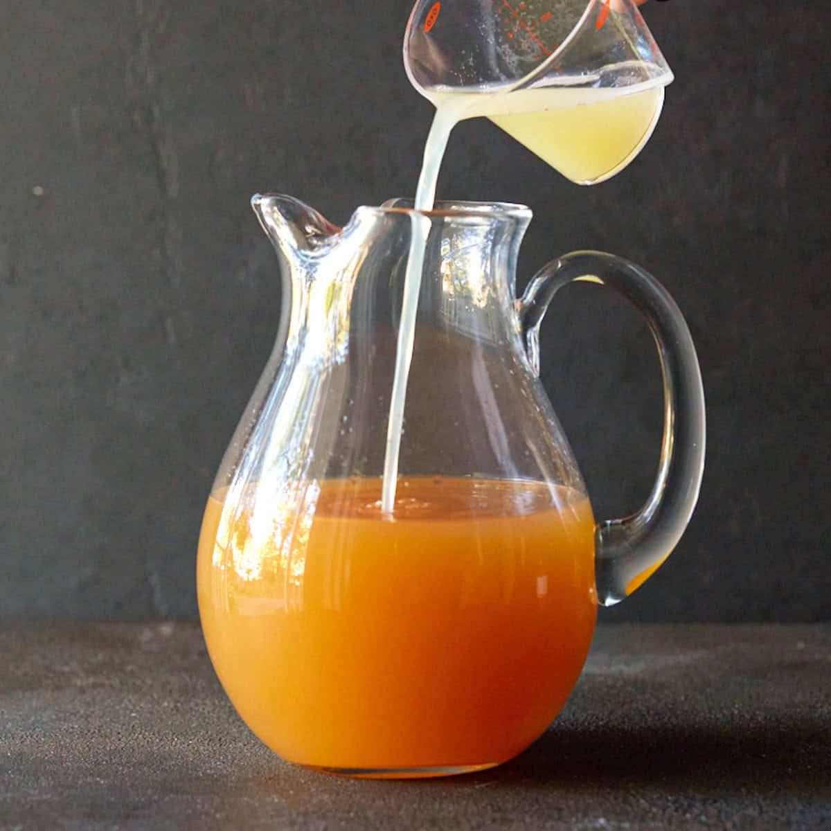 Lemon juice being poured into a glass pitcher of apple cider sangria.