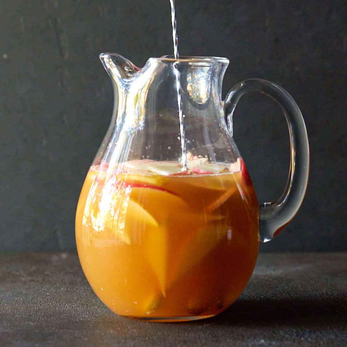 A bar spoon stirring apple cider sangria in a glass pitcher.