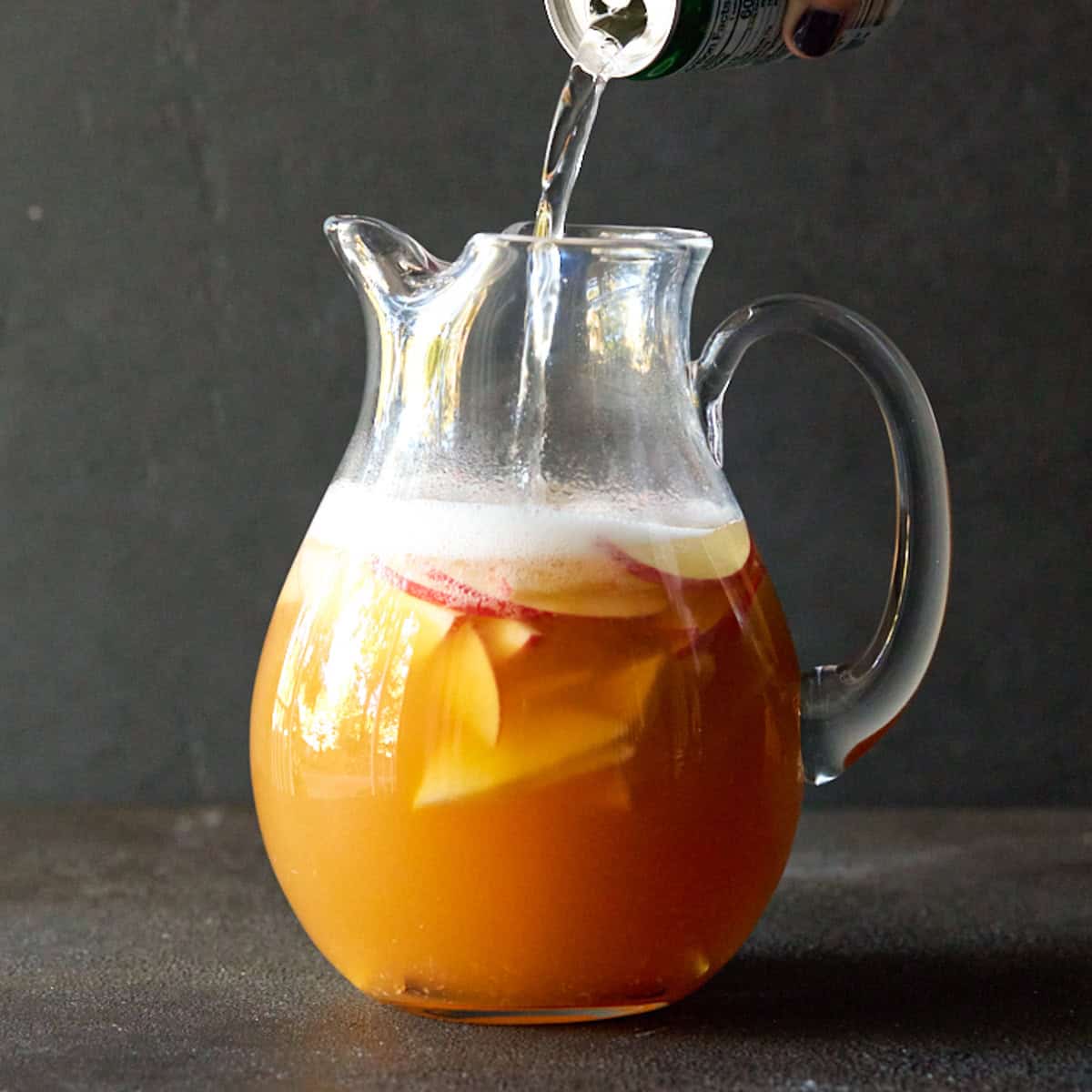 Ginger ale being poured into a glass pitcher of Apple Cider Sangria.