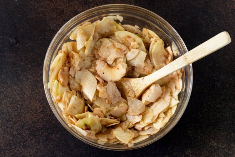 Thinly sliced apples tossed with sugar and cinnamon in a glass bowl.