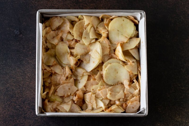 Thinly sliced apples with sugar and cinnamon in an 8x8 metal pan.