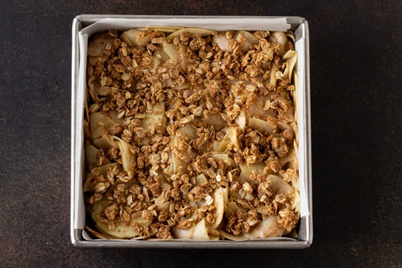 Unbaked apple crisp bars in a parchment-lined 8x8 metal pan.
