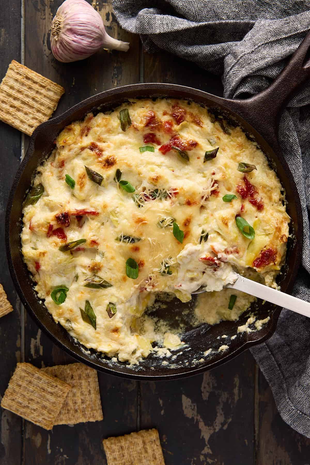 Baked Asiago artichoke dip in a cast iron pan with a scoop removed.