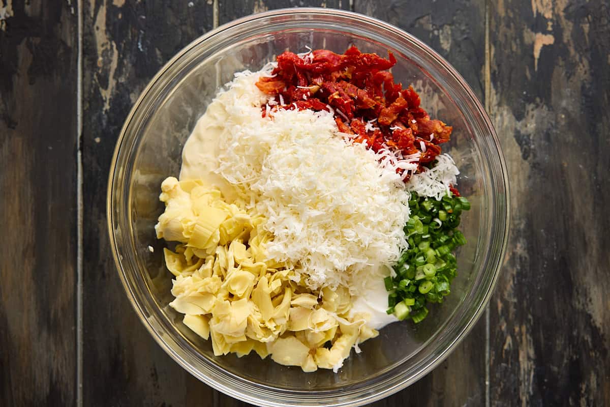Bowl of chopped artichokes, mayo, sour cream, green onions, sun-dried tomatoes and grated cheese.