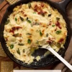Asiago artichoke dip in a black cast iron pan with green onions on top.