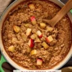 Baked Steel cut oatmeal in a dutch oven with apple chunks and a spoon.