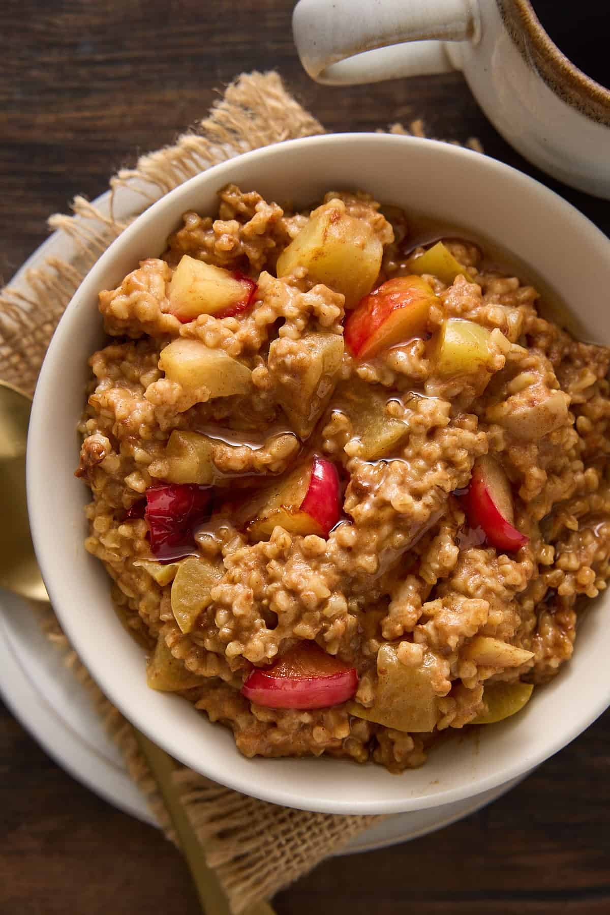 Single bowl of steel cut oatmeal with baked apples and syrup.