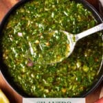 chimichurri on a spoon above a gray bowl.
