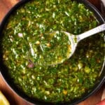 chimichurri in a gray bowl with a lemon and herbs.