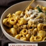 Creamy pumpkin pasta in a beige ceramic bowl with a gold spoon.