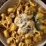 A beige bowl filled with creamy pumpkin pasta with a sausage and sage sauce.