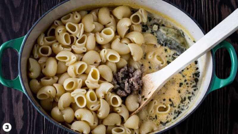Short pasta added to a dutch oven filled with creamy pumpkin sausage sauce.