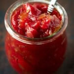 A glass jar with a silver spoon filled with homemade tomato jam.