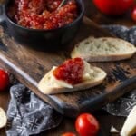 Homemade tomato jam spread on a baguette slice with a white cheese slice.