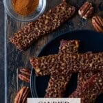 Candied bacon on a wooden tray with cayenne and pecan halves.