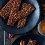 Two plates of candied bacon slices with a small bowl of cayenne.