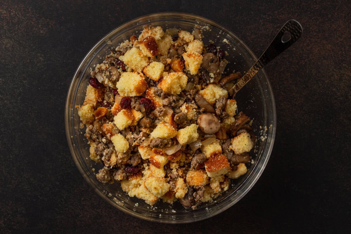 Unbaked cornbread stuffing in a glass bowl with a silver mixing spoon.