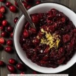 A silver spoon in a white bowl of chunky homemade cranberry sauce topped with lemon zest.
